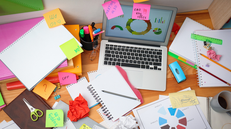 A messy, unorganized desk with post it notes and notebooks scattered around.