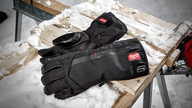 A pair of Milwaukee USB Rechargeable Heated Gloves on a snow-covered work bench