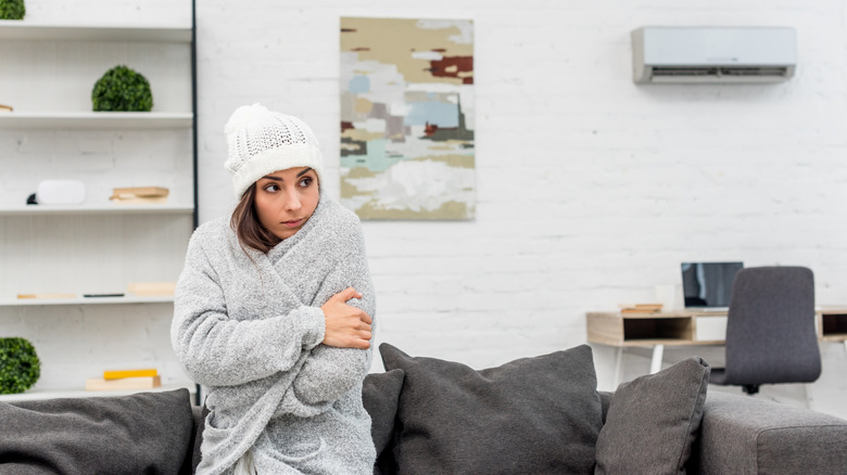 Young woman in warm clothes sitting on the couch at home.