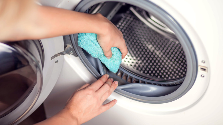 blue-gloved hand wiping washing machine drum 