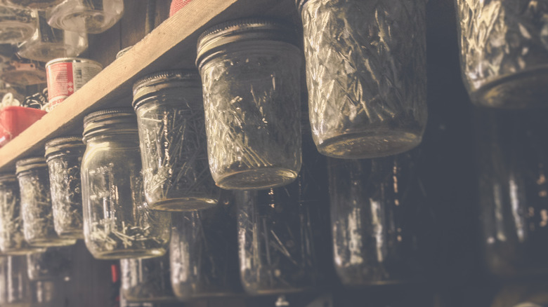 Mason jars filled with nails hanging from underneath wooden shelf