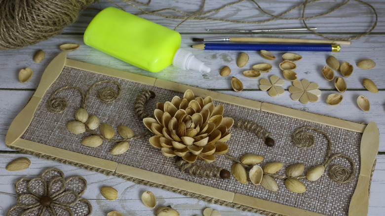 Pistachio shells arranged as a flower on a burlap canvas with crafting supplies sitting at the top.