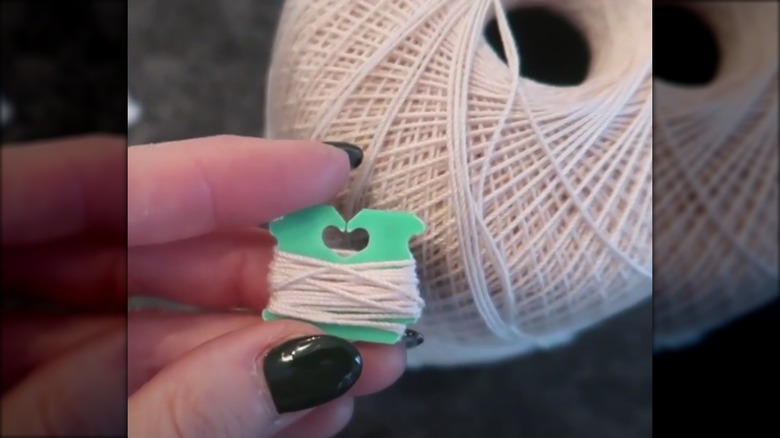 Hand holding a plastic bread tag next to a spool of thread, thread is wrapped around the tag