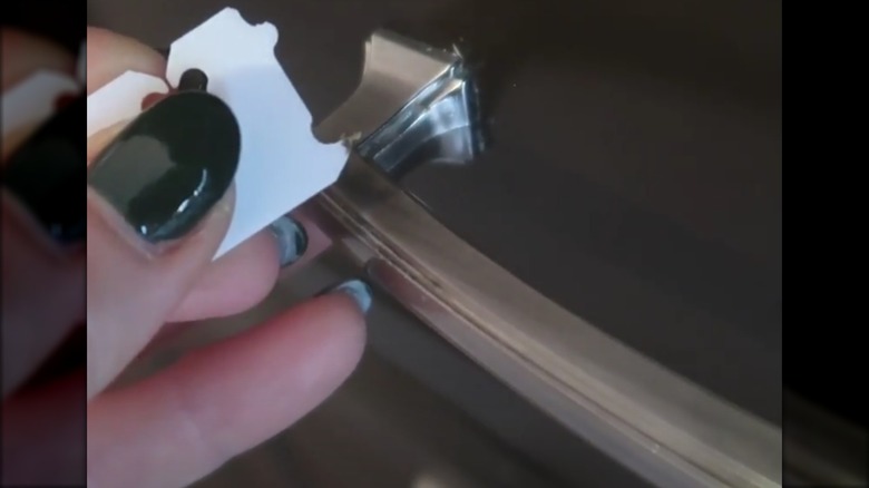 Person using a plastic bread tags to scrape grime from a narrow crack on a drawer handle