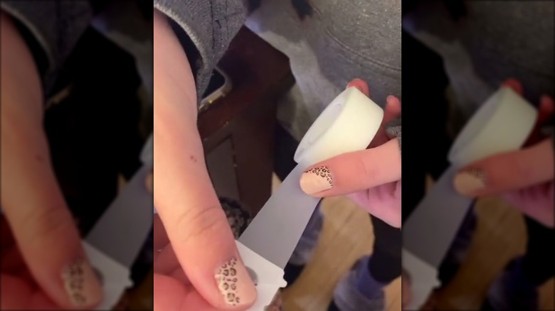 Hands holding a roll of tape with a bread tag on the end to not lose the end of the tape