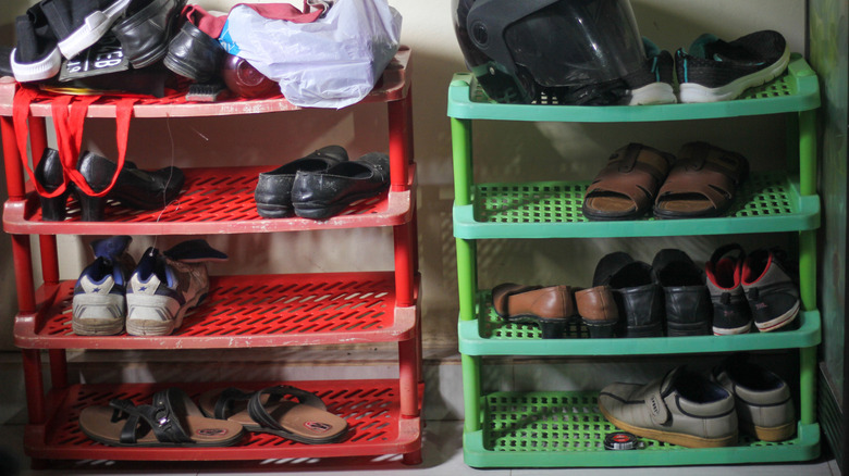 Shoes, a helmet, and other personal items on a red and green shoe rack in a garage.