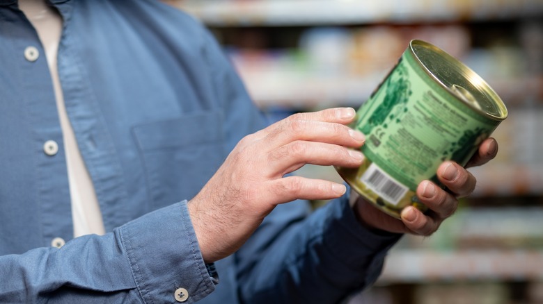 A man holds a food can out from his body while reading the label.