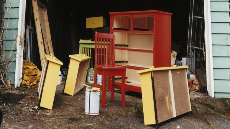 Painted wood furniture sits outside the open door of a garage.