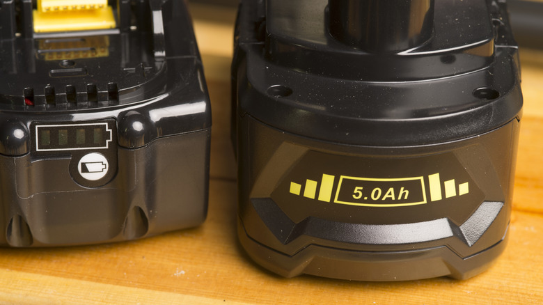 Two lithium ion batteries for power tools sit on a wooden table.