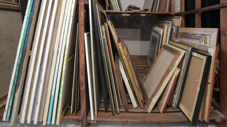 Paintings lie stacked against one another in garage storage shelves.