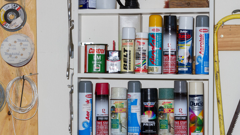 Spray paint and other aerosol cans on a shelf in a garage.