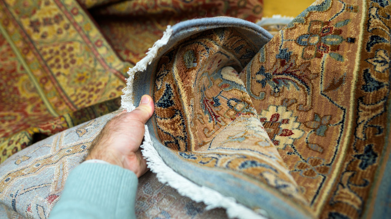 A person pull open one corner of a rug in poor condition.