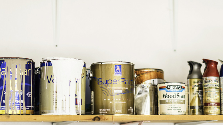 Paint and wood stain cans sit on a shelf in a garage.