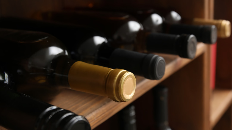 A few bottles of wine are stored lying down on wooden shelves.