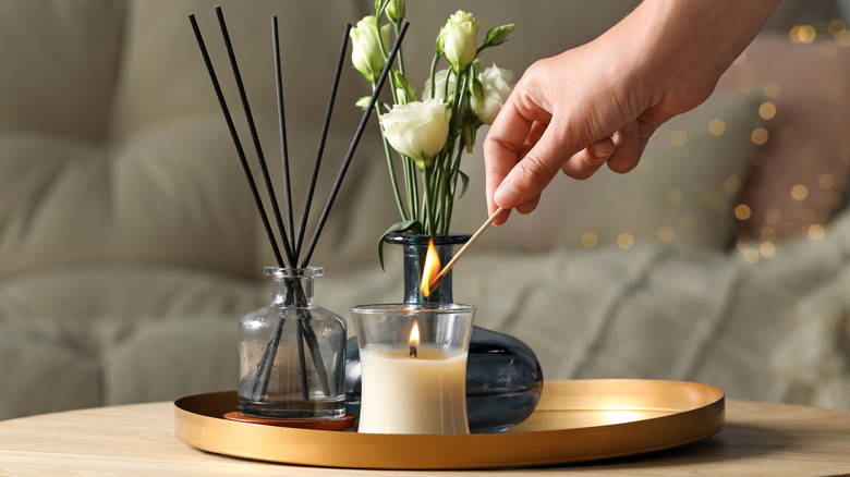 Close up of hand lighting candle with diffuser and flowers in background