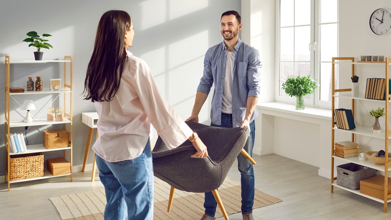 A man and woman lift a gray chair.