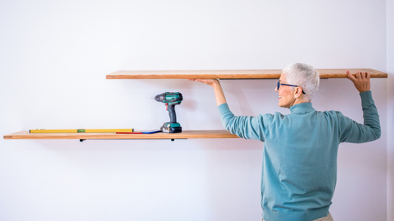 A person mounting large wooden shelves on a white wall