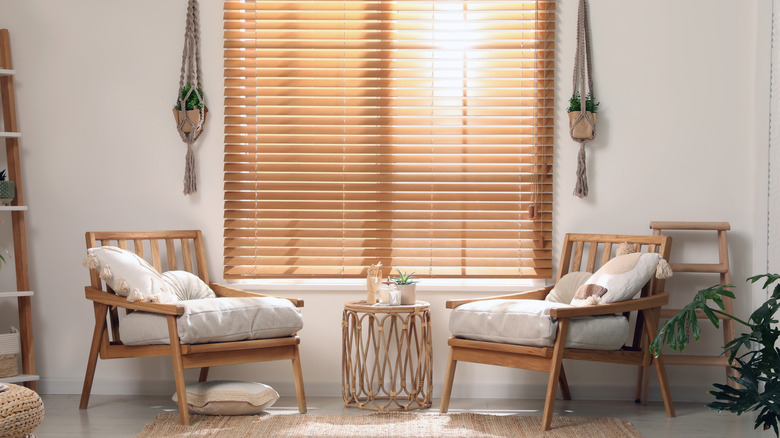 Seating area with two chairs, white pillows, and large window with wood blinds