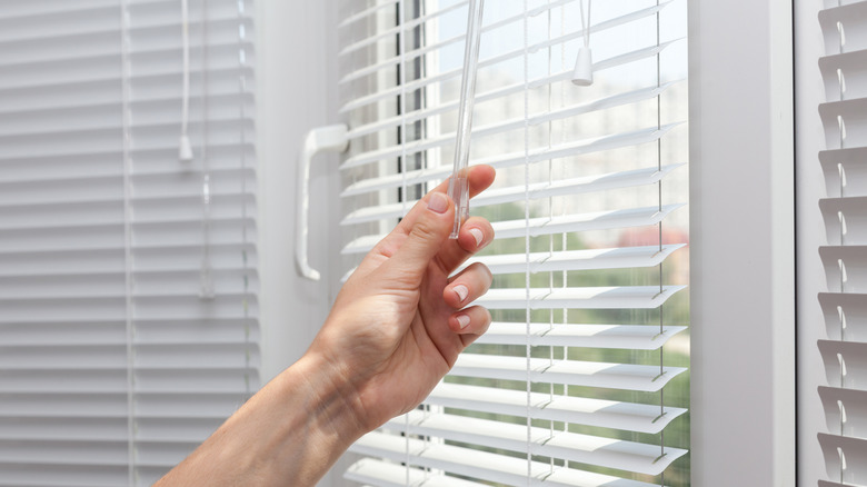 person closing white vinyl window blinds