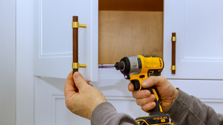 Person installing new wooden cabinet handles with a drill