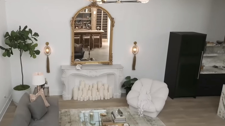 Living room with white fireplace mantel, gilt mirror, white chair, and gray sofa