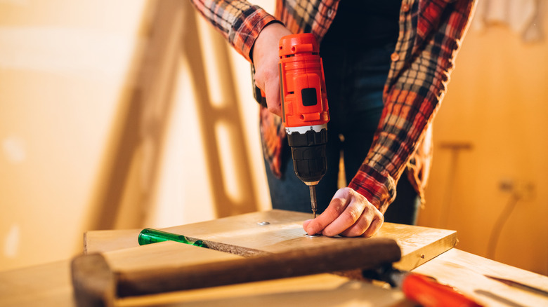 A woman uses a drill on a piece of wood