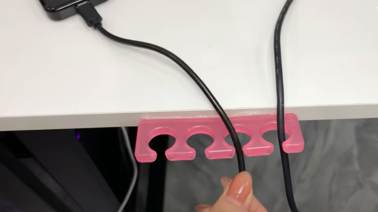 Person uses a pink toe separator to organize black cords behind a desk