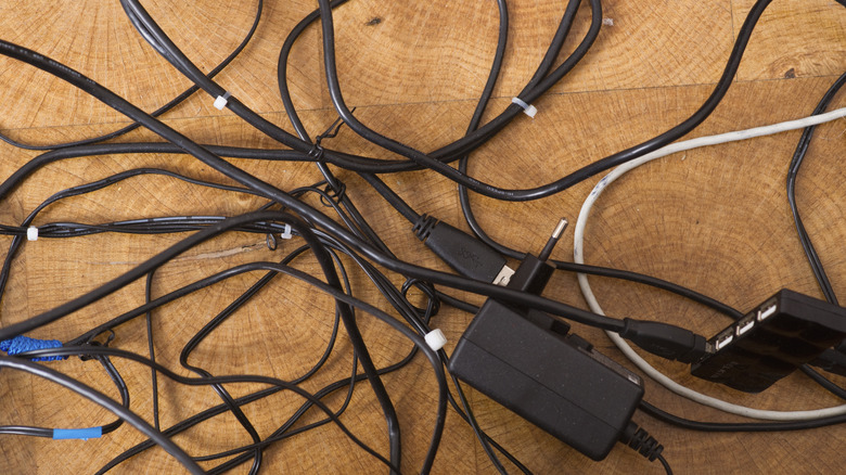 Messy, tangled black cords and computer chargers scattered on a wood desktop