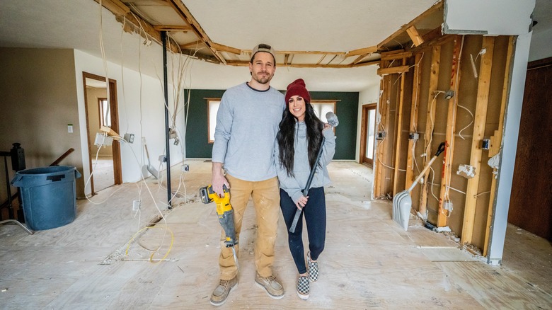 Chelsea and Cole DeBoer holding tools in room they're renovating