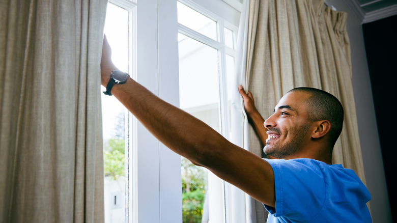 man opening curtains