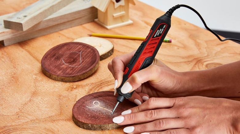 A person using a rotary tool to carve letters on wood