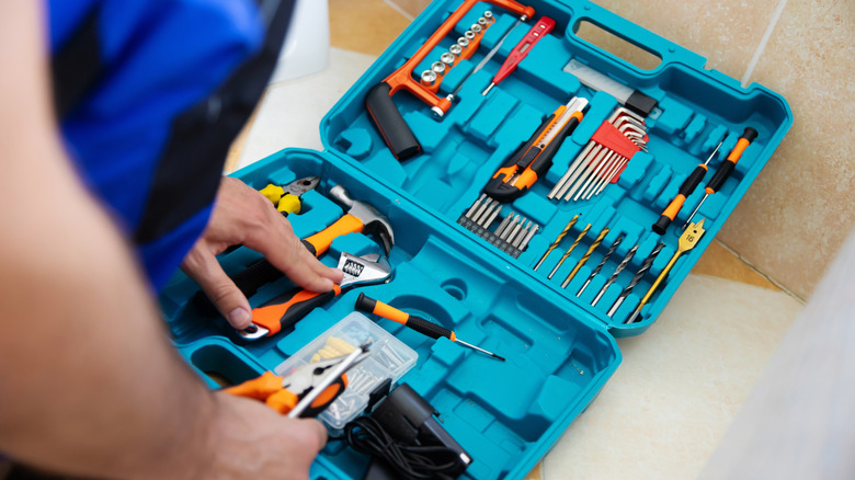 A blue open tool box with slots for individual tools, with a person bending over it