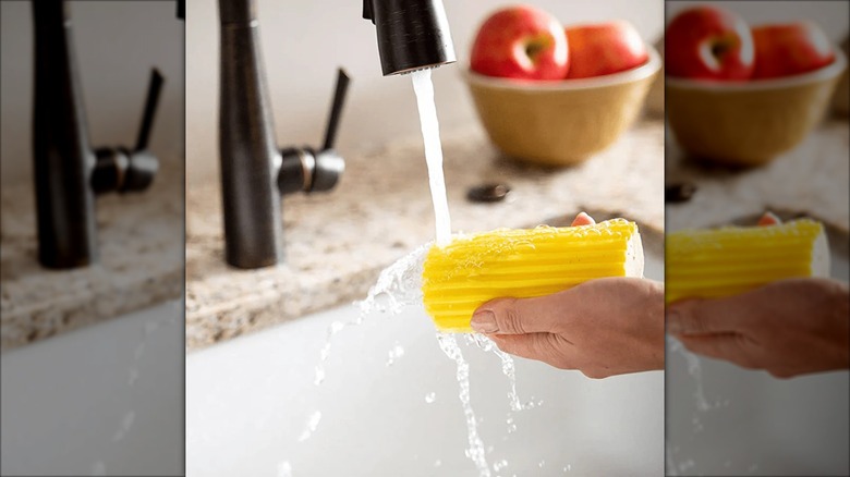 A Scrub Daddy damp duster is held under a faucet