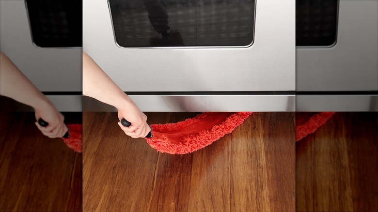 A red microfiber duster is used under an oven