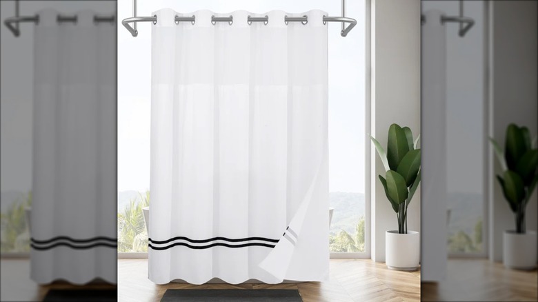 An indoor plant sits next to an elegant white shower curtain with two black stripes