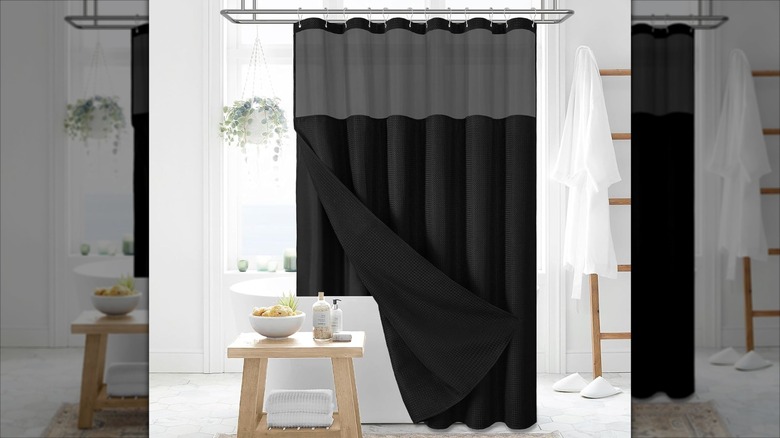 An elegant black shower curtain with black snap-in liner hangs in a white bathroom with light wood accents