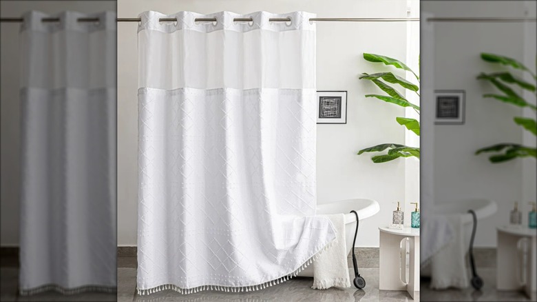 A white boho shower curtain is draped on a freestanding tub