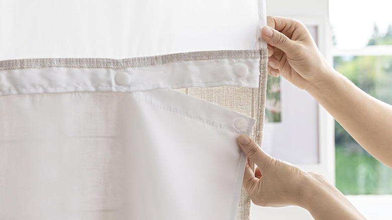 A person removes a white snap-in liner from a beige linen farmhouse style shower curtain