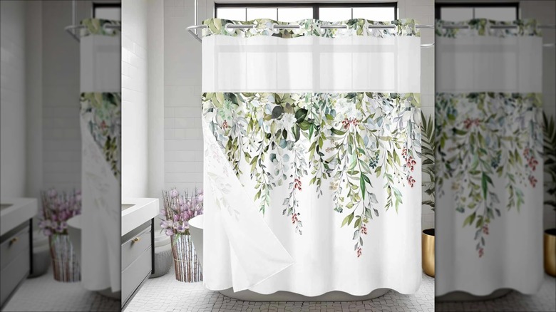 A floral designed shower curtain hangs in front of a white freestanding bathtub