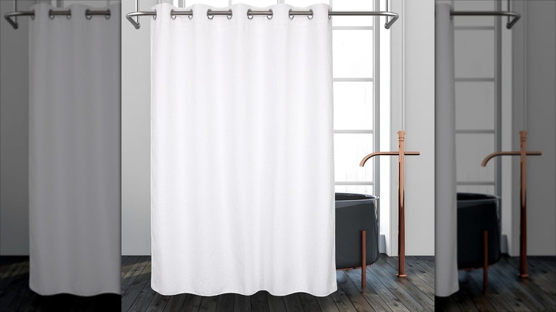 A white shower curtain is shown in an elegant neutral bathroom with a black tub and copper fixtures