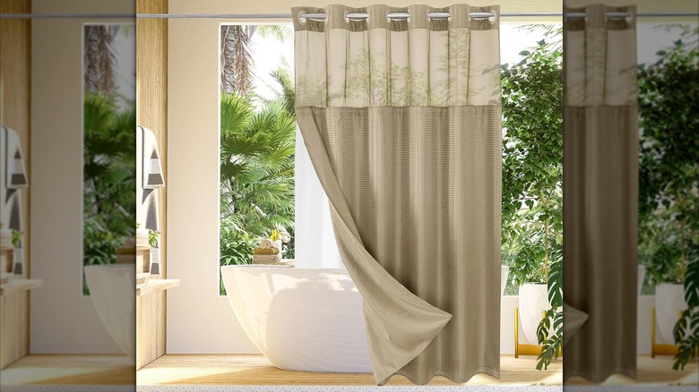 A neutral beige shower curtain is folded back to show the white snap-in liner in a modern and tropical looking bathroom