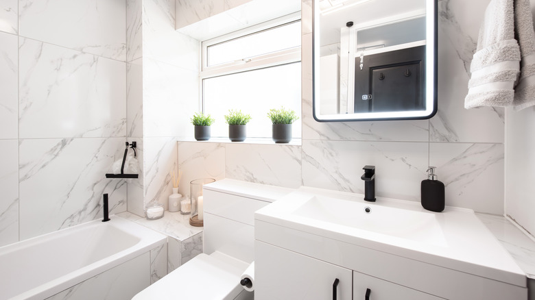 A modern white bathroom is decorated with potted plants and black accents