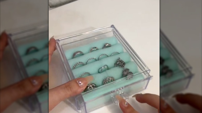 Manicured fingers tapping acrylic box with foam rollers holding rings