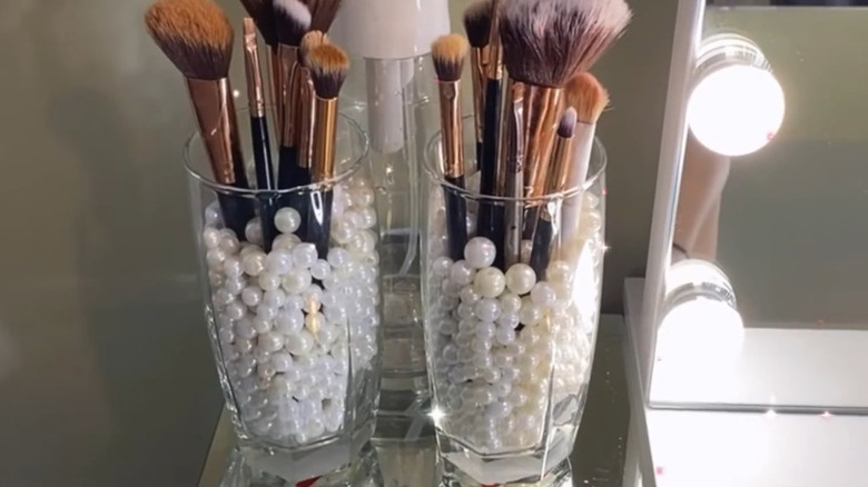 Glass vase filled with white pearls and makeup brushes