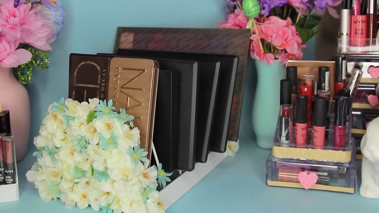 Makeup palettes stacked in a dish rack and decorated with flowers