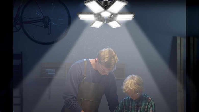 A father and son work together in a garage under a bright multi-panel ceiling light fixture