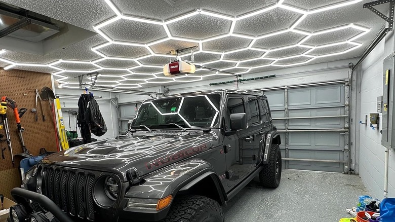 A grey Jeep is parked in a garage lit by a hexagonal ceiling fixture