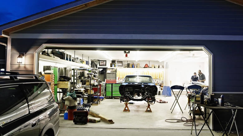 A garage door is open at night to show a brightly lit car workshop