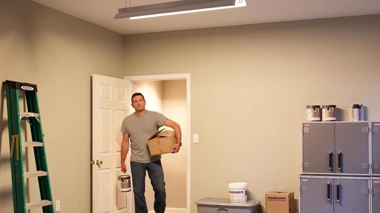 A man carries a box and a paint can into a garage