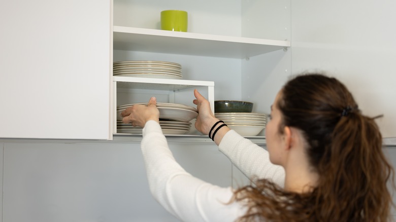 Woman putting dishes in cabinet with shelf risers